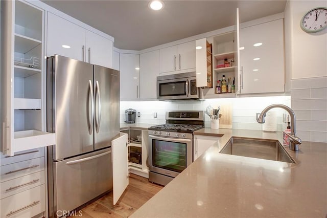 kitchen featuring light wood finished floors, decorative backsplash, stainless steel appliances, open shelves, and a sink