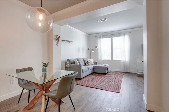 dining area featuring baseboards, light wood finished floors, visible vents, and crown molding