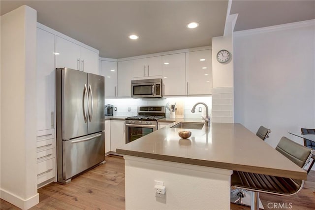 kitchen featuring a peninsula, a sink, white cabinetry, appliances with stainless steel finishes, and light wood finished floors