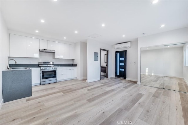 kitchen featuring stainless steel gas range, a wall mounted AC, a sink, under cabinet range hood, and modern cabinets