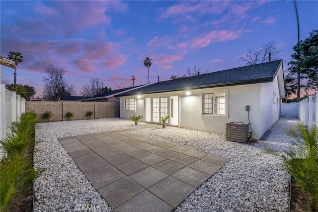 rear view of house with central AC, roof with shingles, stucco siding, a fenced backyard, and a patio area