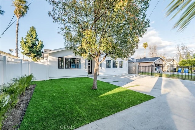 view of front of house with a front yard, concrete driveway, fence private yard, and stucco siding