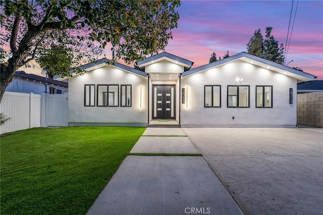 view of front of house with stucco siding, concrete driveway, a front yard, and fence