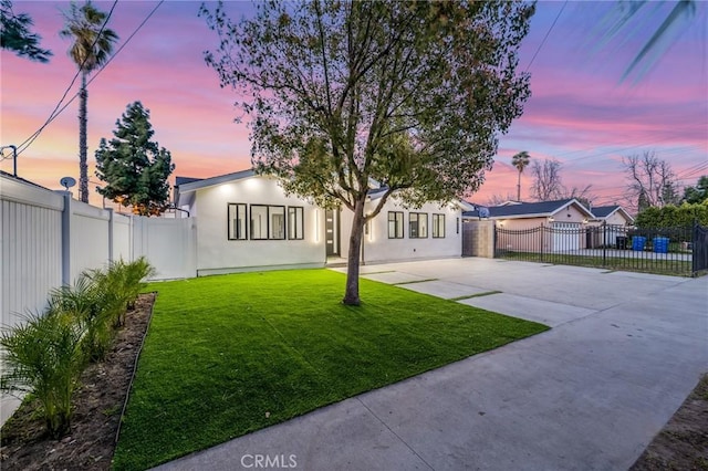 view of front of property featuring fence private yard, a lawn, driveway, and stucco siding