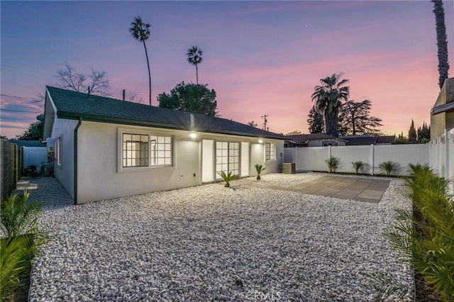 back of property at dusk with a patio area, a fenced backyard, and stucco siding