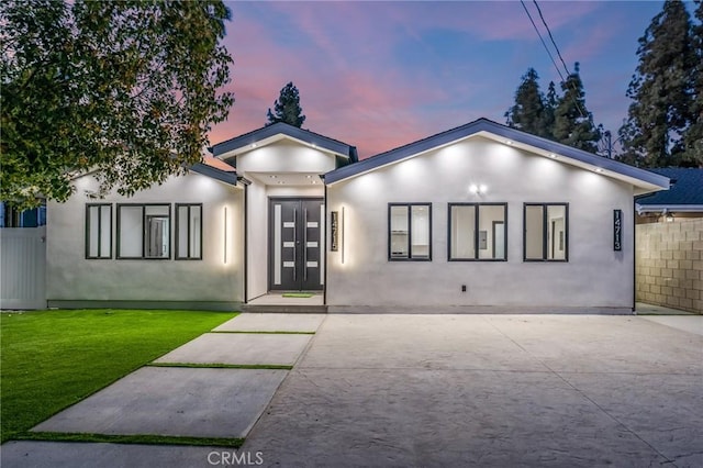 view of front of property with stucco siding, french doors, a front lawn, and fence