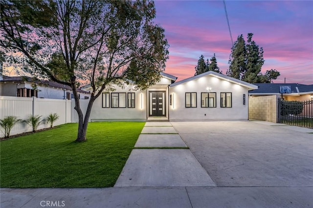 view of front of house featuring a front lawn, fence, driveway, and stucco siding