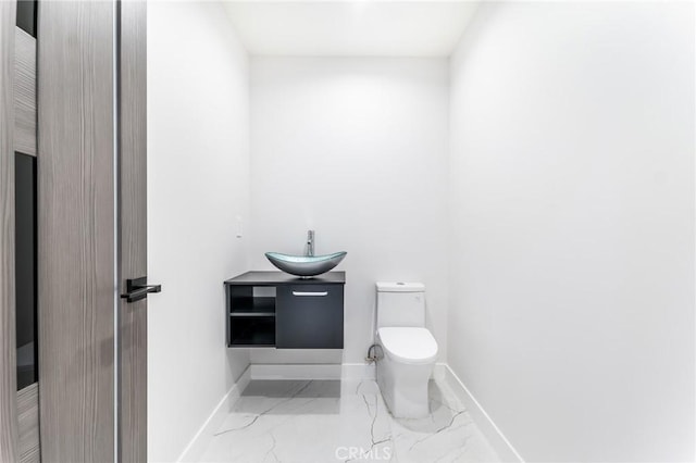 bathroom with marble finish floor, toilet, baseboards, and a sink