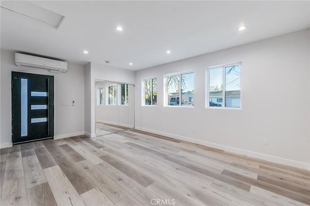 interior space featuring recessed lighting, light wood-style flooring, a wall mounted AC, and baseboards