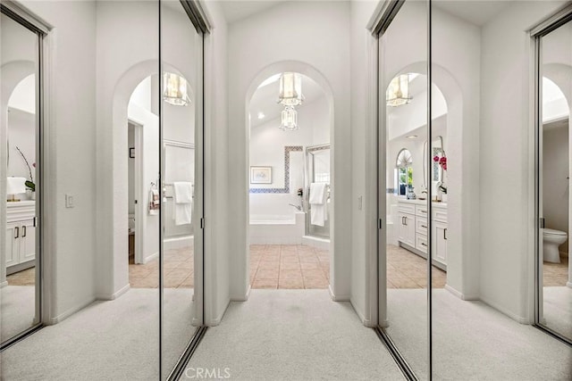 hallway with arched walkways, light carpet, and light tile patterned floors