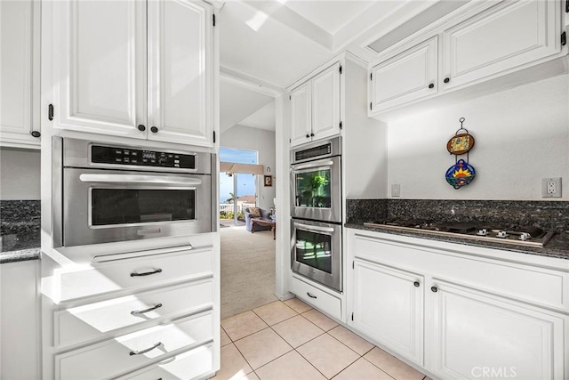 kitchen featuring light tile patterned floors, appliances with stainless steel finishes, dark stone counters, and white cabinetry