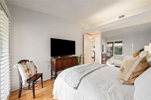 bedroom with a textured ceiling, light wood finished floors, visible vents, and baseboards