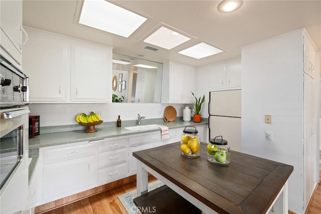 kitchen featuring light wood finished floors, visible vents, freestanding refrigerator, white cabinetry, and a sink