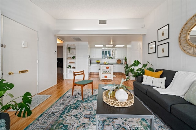 living room with light wood-type flooring, visible vents, and a textured ceiling