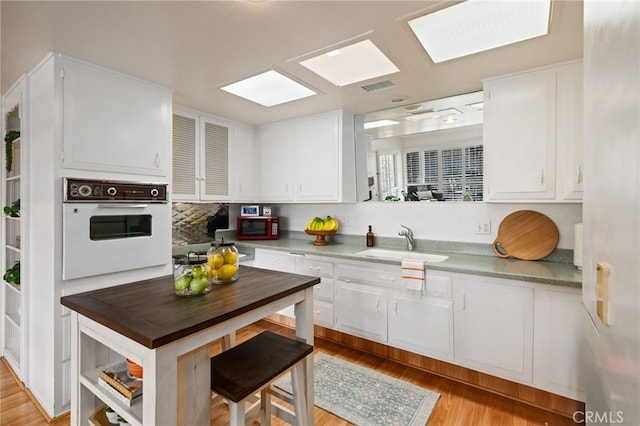 kitchen with white cabinetry, visible vents, a sink, and white oven