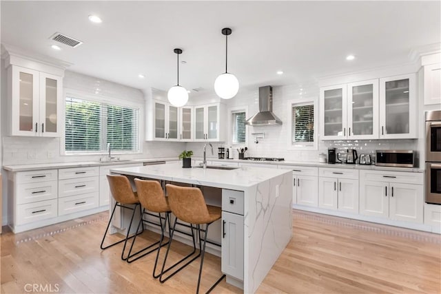 kitchen with light wood-style flooring, stainless steel appliances, a sink, visible vents, and wall chimney range hood