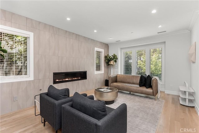 living area with light wood-style floors, a glass covered fireplace, visible vents, and crown molding