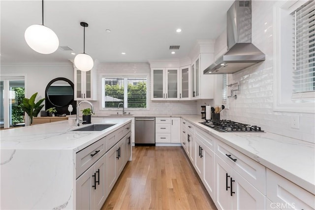 kitchen with wall chimney range hood, a sink, appliances with stainless steel finishes, and white cabinets