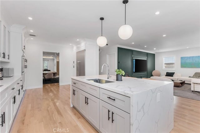 kitchen with light wood finished floors, crown molding, open floor plan, and a sink