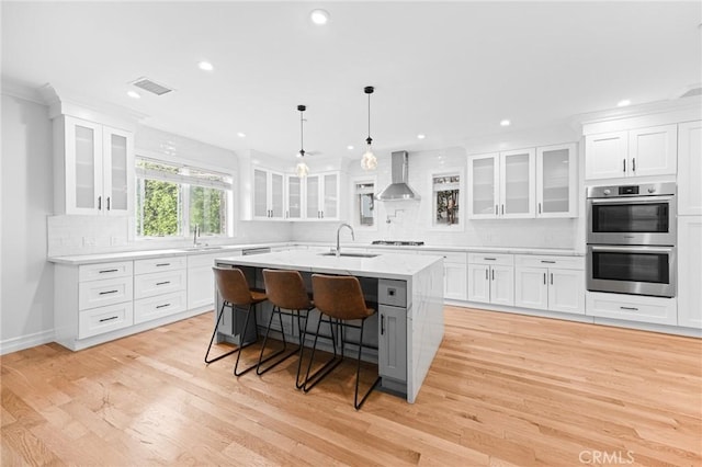 742 N Detroit St, Los Angeles, CA 90046 - kitchen with wall chimney range hood, a sink, stainless steel appliances, white cabinetry, and a center island with sink