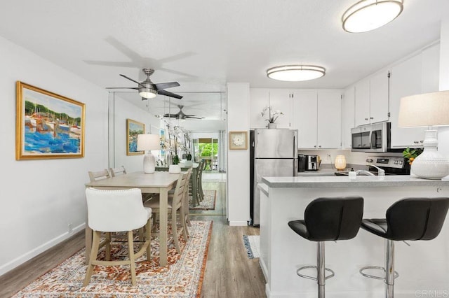 kitchen featuring appliances with stainless steel finishes, light countertops, light wood-type flooring, a kitchen bar, and white cabinetry