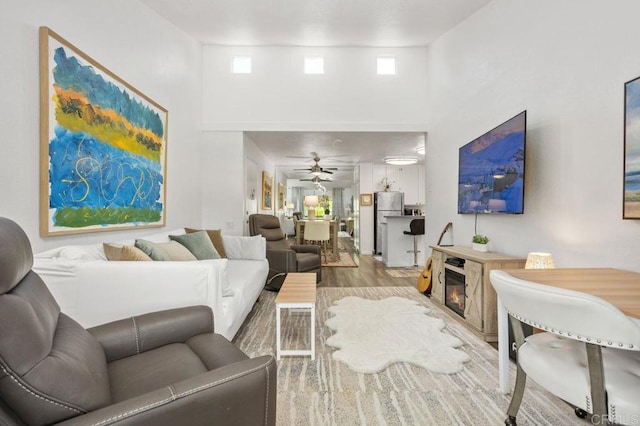 living area with a glass covered fireplace, a high ceiling, wood finished floors, and a ceiling fan