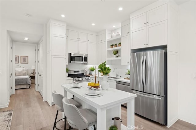 kitchen featuring a sink, white cabinets, appliances with stainless steel finishes, open shelves, and a kitchen bar