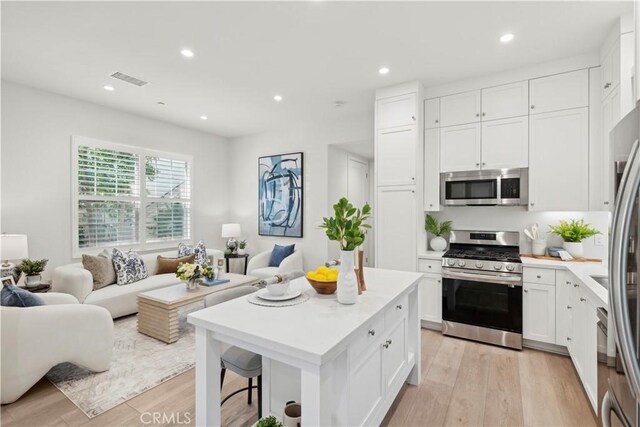 kitchen with stainless steel appliances, light countertops, light wood-style floors, open floor plan, and white cabinetry