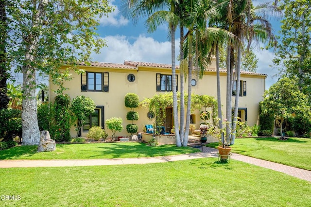 view of front of house with a front yard, a tile roof, and stucco siding