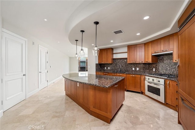 kitchen with brown cabinetry, a kitchen island, white oven, under cabinet range hood, and stainless steel gas cooktop