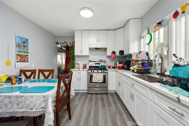 kitchen with a sink, white cabinetry, light countertops, stainless steel gas range, and light wood finished floors