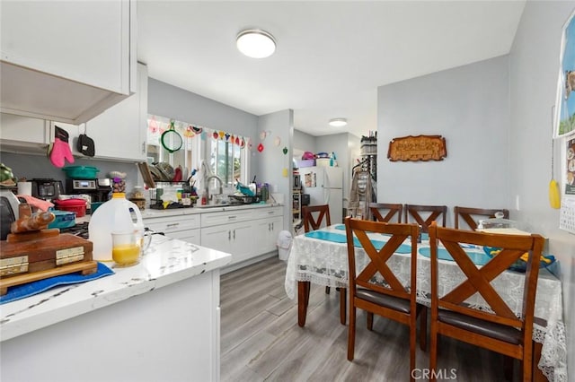 kitchen featuring light wood-type flooring, freestanding refrigerator, white cabinetry, and a sink