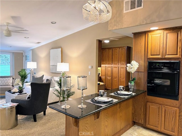 kitchen with ornamental molding, brown cabinetry, dark stone counters, black oven, and a peninsula