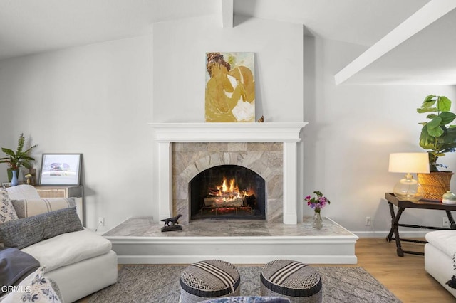 living area featuring baseboards, wood finished floors, vaulted ceiling with beams, and a tile fireplace