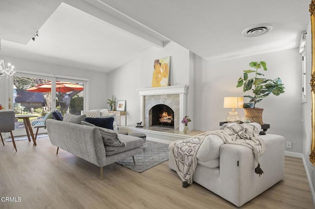 living room with a high end fireplace, visible vents, an inviting chandelier, and wood finished floors