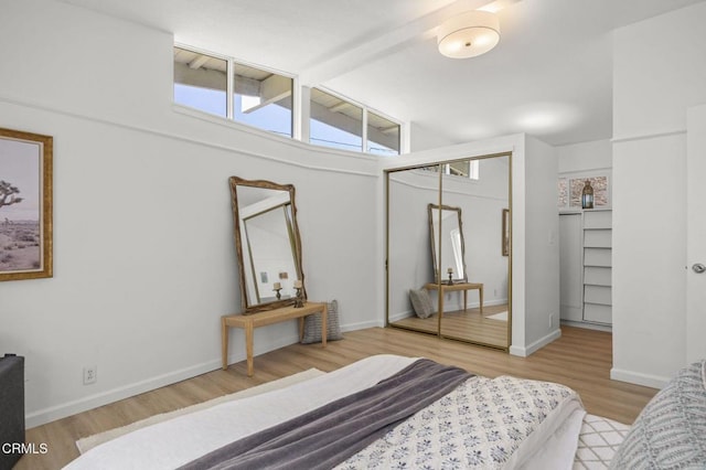 bedroom with a closet, light wood finished floors, vaulted ceiling with beams, and baseboards