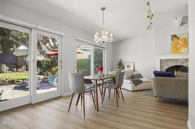 dining room featuring a warm lit fireplace, light wood-style flooring, and an inviting chandelier