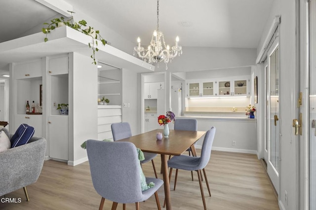 dining room featuring a notable chandelier, baseboards, lofted ceiling, and light wood-style floors