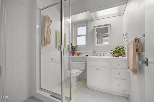 bathroom featuring vanity, toilet, a stall shower, and wainscoting