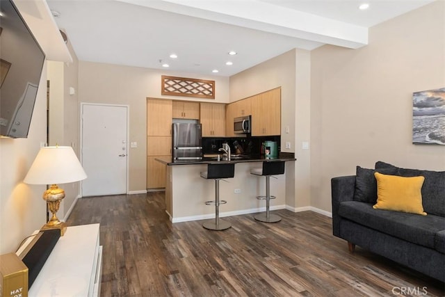 kitchen featuring light brown cabinets, stainless steel appliances, a peninsula, open floor plan, and dark countertops