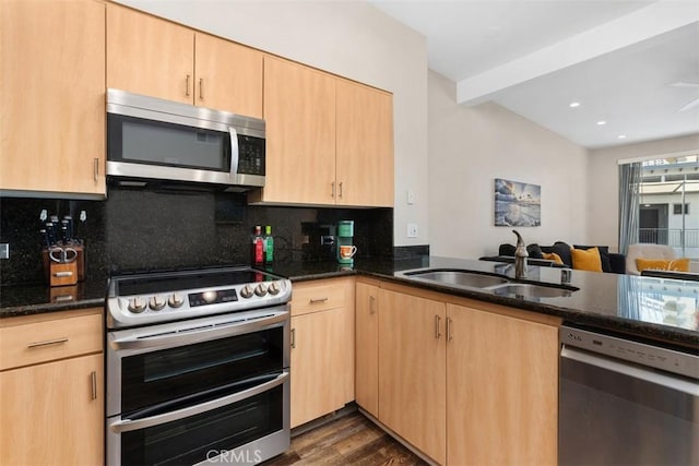 kitchen featuring light brown cabinets, stainless steel appliances, dark stone countertops, and a sink