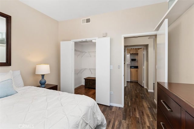 bedroom featuring visible vents, baseboards, a spacious closet, a closet, and dark wood-style floors