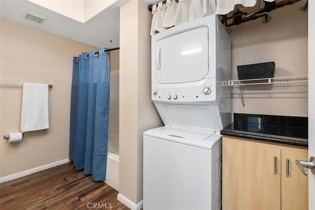 clothes washing area featuring dark wood-style floors, visible vents, stacked washer / dryer, laundry area, and baseboards