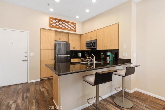 kitchen with dark wood-style floors, a peninsula, stainless steel appliances, light brown cabinets, and a sink