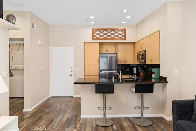 kitchen featuring dark wood-style flooring, stainless steel appliances, stacked washer and dryer, visible vents, and a peninsula