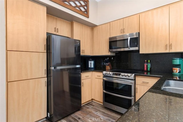 kitchen with stainless steel appliances, tasteful backsplash, dark stone countertops, and light brown cabinetry