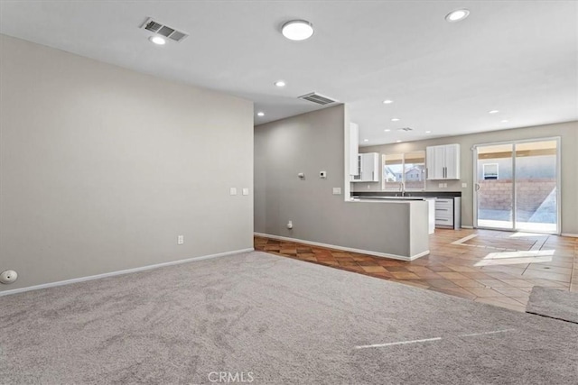 unfurnished living room featuring light carpet, a sink, and visible vents