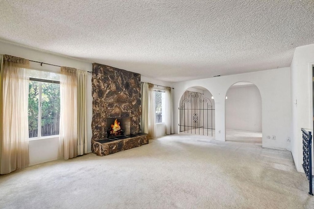 unfurnished living room featuring carpet floors, arched walkways, a fireplace, and a textured ceiling