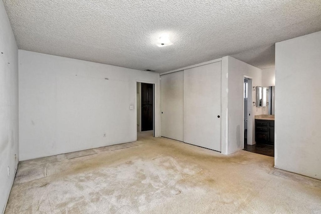 unfurnished bedroom with visible vents, ensuite bathroom, a textured ceiling, carpet floors, and a closet