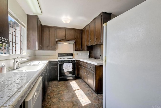 kitchen featuring range with gas stovetop, tile countertops, freestanding refrigerator, under cabinet range hood, and a sink